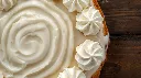 Generate an image of Tres-leaches pastry fully white poured with milk and piped with whipping cream plated in wooden table (1).webp