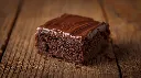 Generate an image of  double chocolate fudge brownie topped with chocolate layer in wooden table (1).webp